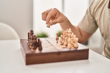 Young man playing chess sitting on table at home