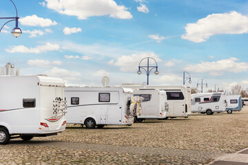 Many white modern campervan recreational motor home vehicles parked in row at camper park site Magdeburg city against Elbe river bridge. Motorhome campground stataion travel destination. RV lifestyle