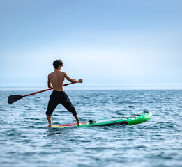 Fototapeta na wymiar a sporty guy swims on a sup board with a paddle on the sea during the day against a beautiful sky
