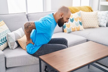 Young bald man suffering for backache sitting on sofa at home