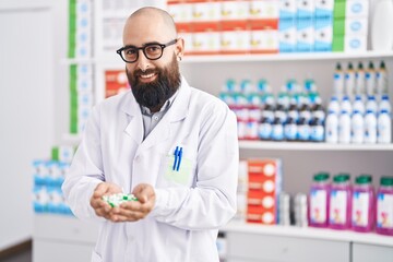 Young bald man pharmacist smiling confident holding pills at pharmacy