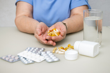 Senior woman with wrinkled old hands at the table holding different capsules and vitamins, full palms with pills for treatment. Healthcare and medicine concept