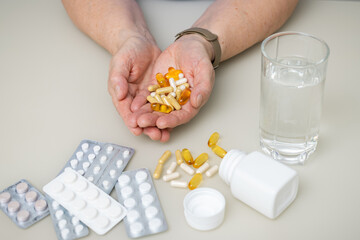Senior woman with wrinkled old hands at the table holding different capsules and vitamins, full palms with pills for treatment. Healthcare and medicine concept