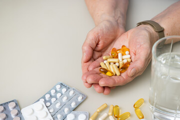 Obraz premium Senior woman with wrinkled old hands at the table holding different capsules and vitamins, full palms with pills for treatment. Healthcare and medicine concept