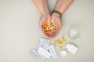 Obraz premium Senior woman with wrinkled old hands at the table holding different capsules and vitamins, full palms with pills for treatment. Healthcare and medicine concept, top view