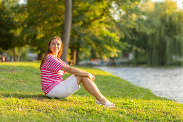 Naklejka na ściany i meble Beautiful woman resting and relaxing sitting on the grass in a park