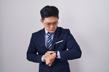 Young asian man wearing business suit and tie checking the time on wrist watch, relaxed and confident