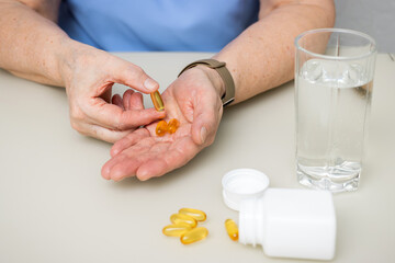 Senior woman with wrinkled old hands at the table holding omega 3 yellow capsules, fish oil pills, Healthcare and medicine concept