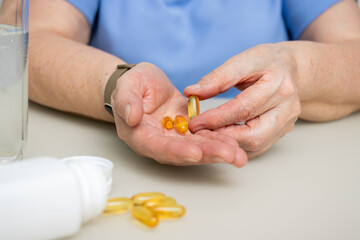 Senior woman with wrinkled old hands at the table holding omega 3 yellow capsules, fish oil pills, Healthcare and medicine concept
