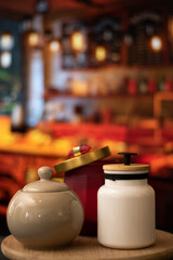 Vertical view of Mugs of sugar and salt containers style vintage over a table in night restaurant with selective focus and bokeh background