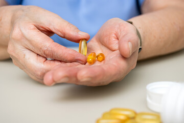 Senior woman with wrinkled old hands at the table holding omega 3 yellow capsules, fish oil pills, Healthcare and medicine concept