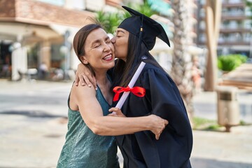 Two women mother and graduated daughter holding diploma kissing at street
