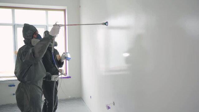 Airless Spray Painting. Two painters in protective gear paint a wall with an airless spray gun.