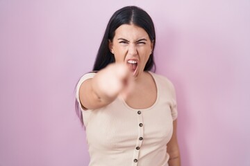 Young hispanic woman standing over pink background pointing displeased and frustrated to the camera, angry and furious with you