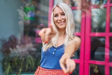 Young blonde woman smiling confident pointing with fingers at street