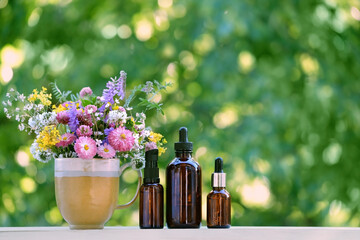 amber glass bottles of herbal essential extract, oils and flowers in cup on table close up,...