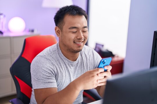 Young chinese man streamer using computer and smartphone at gaming room
