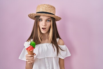 Teenager girl holding ice cream in shock face, looking skeptical and sarcastic, surprised with open mouth