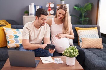 Man and woman couple expecting baby using laptop and calculator accounting at home