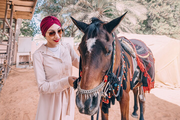 In the dusty desert, a girl with a flowing dress gently leads her Arabian horse, their bond...