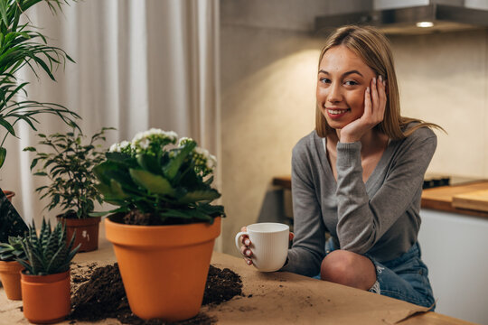 A Cute Caucasian Woman Is Looking At The Camera With Lots Of Houseplants On The Table In Front Of Her