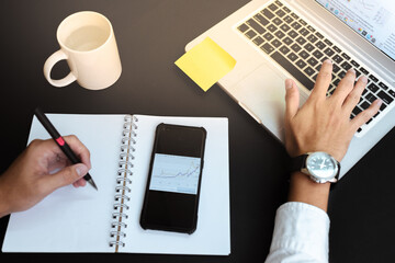 Hand of a businessman scrolling the pad of his laptop for investment planning. Wrist watch attached to hand, and book under his arm. 