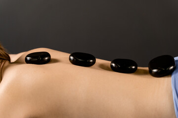 Hot stones for massage therapy close-up. Heated stones are placed on back of young woman for relax and ease tense muscles and damaged soft tissues of body.