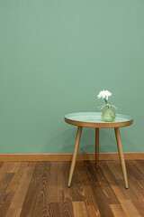 Innenausstattung eines Raumes mit einem kleinen, runden, grünen Tisch auf dem eine Vase mit  weißer Blume vor einer  grünen Wand auf dunkelbraunem Parkett steht, Hochformat