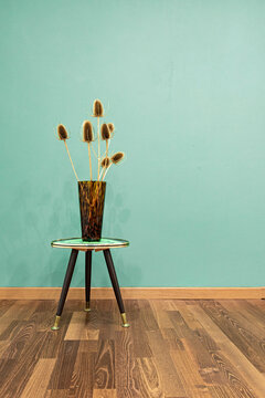Die Innenausstattung eines Raumes im vintage Look 50er - 60er Jahre mit getrockneten Pflanzen in einer braunen Vase auf einem kleinen Tisch vor einer gr&uuml;nen Wand
