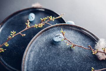 Easter pottery decoration. Close up of dishes with eggs, feathers and spring branches. Ceramic plates on grey.