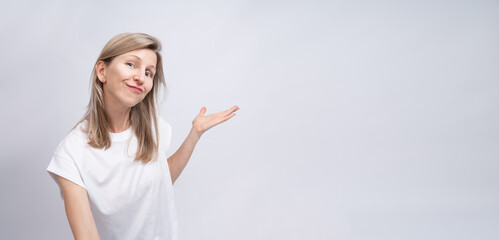 Smiling blonde woman pointing side showing information on long horizontal grey background banner.  White clothe t-shirt and solid gray background