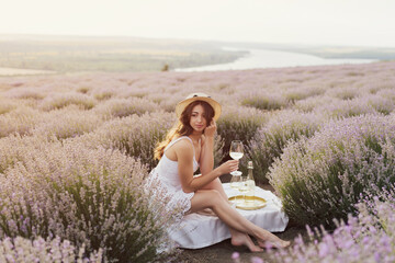 Fototapeta na wymiar Calm and relaxed woman is sitting on the lavender field with beautiful landscape on background. She enjoying beautiful moment. Background sunset. Holidays