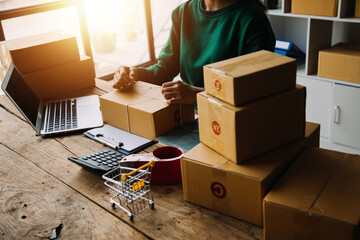 Fototapeta premium SME entrepreneur Small business entrepreneurs Online selling ideas,Happy Young Asian business owner work on computer and a boxs at home,delivery SME procurement package box deliver to customers,