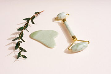Cosmetic background roller for the face, anti-aging scraper guasha eucalyptus leaves. Pastel pink background skin care set.