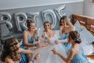 Young bridesmaids in blue silk dresses drink champagne in the bride's room. Beautiful women...