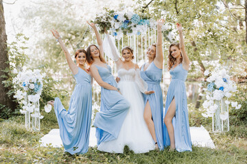 The bridesmaids in blue dresses raise their hands, rejoice, the bride is holding a beautiful...