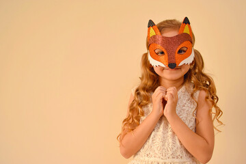 A child in a masquerade carnival mask of a fox, hand-made from glitter foamiran. Little cute cheerful comical girl in the role of a fox. The child is preparing for the carnival, holidays.