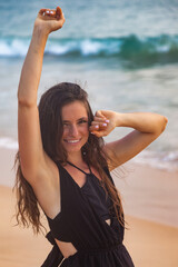 Happy pretty young smiling woman posing on seacoast looking at camera at ocean waves background, summer vacation. Lovely beautiful lady on resting, travel lifestyle. Tropic holiday concept. Copy space