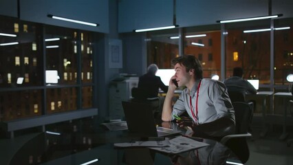 Young manager talk on phone working late in loft office with night city view outside windows