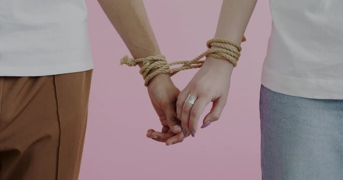 Close-up of hands tied with rope touching expressing love in committed relationship on pink color background. People and connection concept.