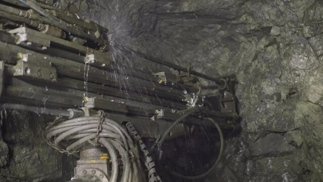 Robot drill makes hole for setting explosives in hard rocks spraying cold water. Heavy machinery equipment with coolant operates in ore mine closeup