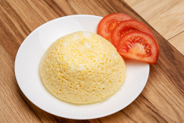 Airy tender egg omelette on a white plate with chopped tomatoes. 