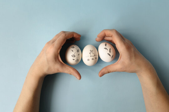 Woman's hands make a heart on the background of painted Easter eggs on a blue background. Easter holiday, minimalism, spring composition.