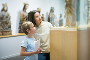 Young woman with son observing with interest sculptures exhibition in art museum, pointing to something interesting - Powered by Adobe