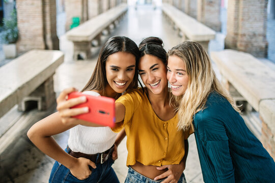 Happy diverse young woman friends enjoying time taking selfie portrait with mobile phone camera. Female friendship concept with three millennial ladies having fun at summer vacation.
