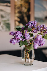 A bouquet of lilacs in a glass vase against the backdrop of large photographs.