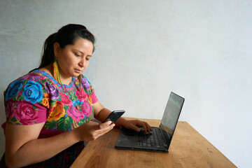Guatemalan woman in traditional huipil dress working with laptop and smartphone