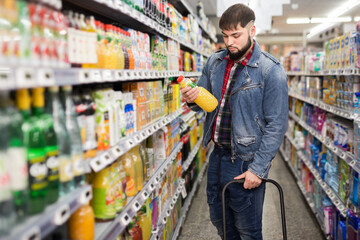 Portrait of focused young man purchasing sweet soft drinks in food store