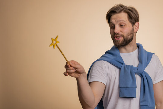 Man magician wizard gesturing with magic wand fairy stick, making wish come true, casting magician spell, advertising holidays sale discount. Young bearded guy isolated on beige studio background