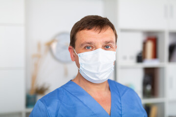 Fototapeta na wymiar Close up portrait of male doctor wearing disposable face mask in medical office